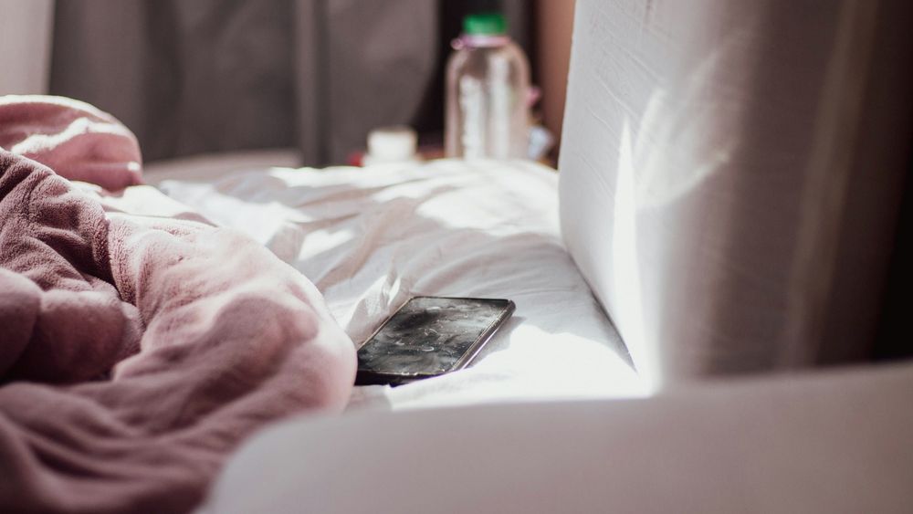 Un telefono appoggiato su un letto disfatto, nella luce del mattino