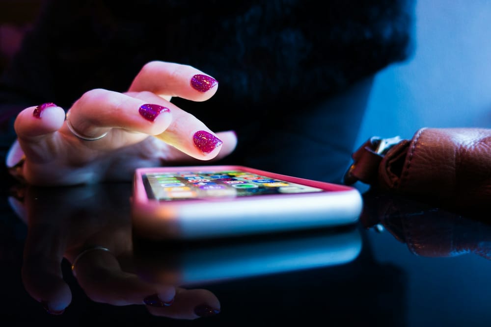 Une main tendue vers un iPhone posé sur une table, écran allumé avec des applications visibles